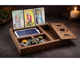 May include: A wooden tarot card box with compartments for cards, crystals, and a lid. Three tarot cards are displayed, along with a deck of cards. The box is made of dark wood and has a celestial design on the lid.
