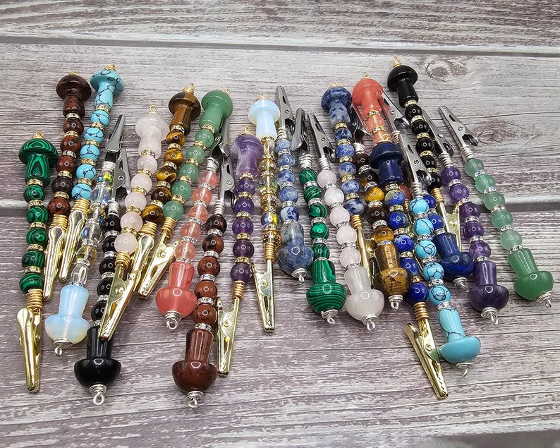 May include: A collection of 18 colorful gemstone and crystal topped, gold-toned, metal hair clips. The clips are adorned with various gemstones, including amethyst, turquoise, tiger's eye, and rose quartz.