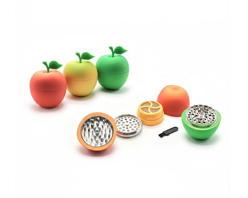May include: A selection of colourful apple-shaped herb grinders in red, yellow, and green. The grinders are shown disassembled, revealing the internal components, including a metal grinding surface and a small black brush.