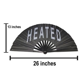 以下が含まれることがあります： 白い「HEATED」の文字が書かれた黒い折りたたみ式の扇子。扇子は幅66cm、高さ33cmです。