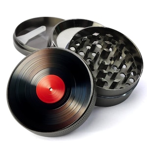 May include: A silver metal grinder with a black vinyl record design on the top. The grinder has three sections, one with a black vinyl record design, one with a screen, and one with a series of teeth.