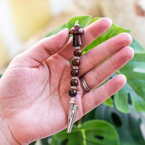 May include: A brown and silver beaded clip with a mushroom charm. The clip is made of metal and has a spring-loaded mechanism. The beads are brown and have a speckled pattern. The mushroom charm is brown and has a white stem.