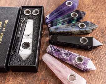 Pode incluir: Uma coleção de cachimbos de pedras preciosas naturais em várias cores, incluindo branco, roxo, preto e cinza iridescente. Cada cachimbo possui um fornilho de metal. Uma caixa de presente preta com o rótulo Natural gemstone smoking pipes está incluída.