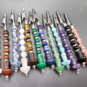 May include: Twelve colorful beaded hair clips with metal clips. Each clip has a different color and pattern of beads, including blue, green, red, purple, and white.