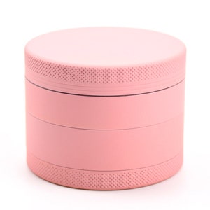 May include: A four-piece pink metal grinder with a textured top and bottom.
