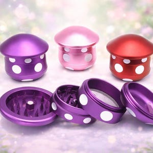 May include: Three mushroom-shaped grinders in purple, pink, and red, each with white polka dots. The grinders are disassembled, revealing their internal components. The design is whimsical and colorful.