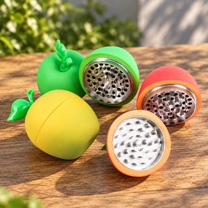 May include: A collection of three apple-shaped herb grinders in bright green, yellow, and red. Each grinder features a smooth, rounded exterior with a small green leaf stem on top and a metallic interior with sharp, perforated teeth for grinding.