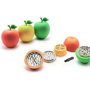 May include: A selection of apple-shaped herb grinders in red, yellow, and green. The grinders are taken apart, showing the metal grinding parts and a small brush. The design is fun and colourful.