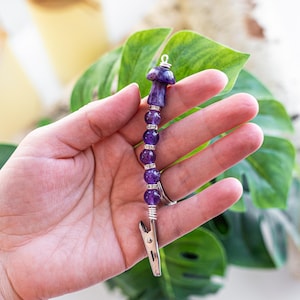 May include: A purple amethyst mushroom charm with a silver clip. The charm is made with amethyst beads and a silver wire.