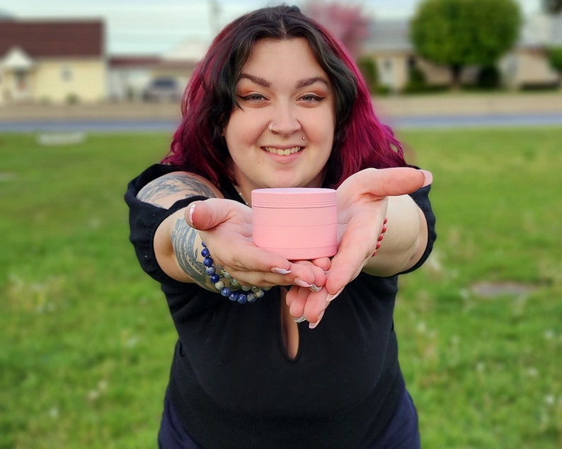 May include: A person is holding out a pink, three-tiered, round container. The container is made of plastic and has a smooth surface.