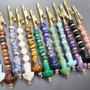 May include: Twelve colorful beaded and gold-toned metal clips. Each clip has a different color scheme of beads, including green, blue, purple, pink, and brown.