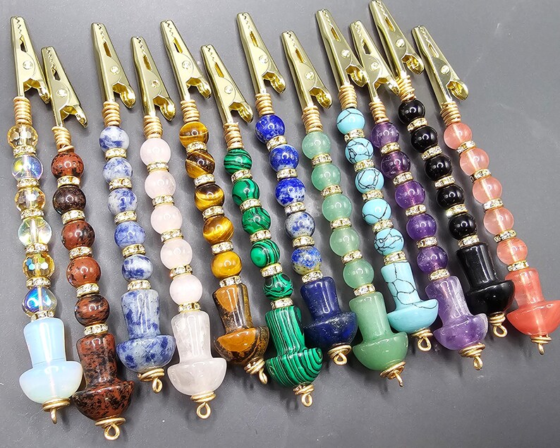 May include: Twelve colorful beaded and gold-toned metal clips. Each clip has a different color scheme of beads, including green, blue, purple, pink, and brown.