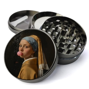 May include: A four-piece, gunmetal-colored herb grinder. The top lid features a print of the painting "Girl with a Pearl Earring" by Johannes Vermeer, with the girl blowing a bubblegum bubble. The grinder has a mesh screen and diamond-shaped teeth.