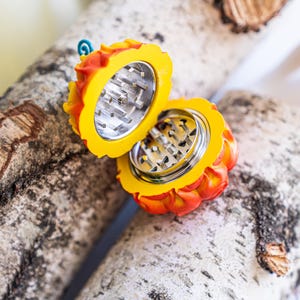 May include: A yellow and orange grinder shaped like a pumpkin with a metal grinding mechanism. The grinder is open and the metal grinding mechanism is visible.