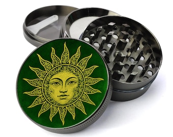 Può includere: Un macinino per erbe in metallo a quattro pezzi, smontato. La parte superiore presenta uno sfondo verde con un disegno di volto di sole giallo. Il macinino è realizzato in metallo grigio scuro e include un setaccio e un raccoglitore di kief.