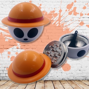 May include: A white and orange grinder with a cartoon character design. The grinder has a removable lid and a metal grinding chamber. The character has a straw hat with a red band.