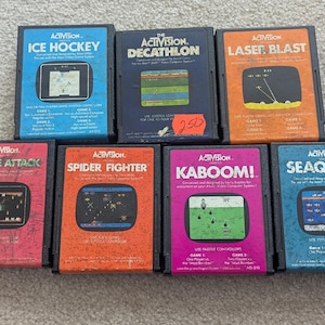 Puede incluir: Una colección de siete cartuchos de videojuegos Activision vintage, incluyendo "Ice Hockey", "Decathlon" y "Laser Blast". Cada cartucho presenta etiquetas coloridas con gráficos y títulos de juegos. Los cartuchos están en sus estuches originales.