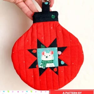 Puede incluir: Monedero rojo en forma de adorno con un diseño de estrella negra y un gráfico de oso polar. El monedero tiene una parte superior negra con un cierre plateado y el texto "ORNAMENT COIN PURSE". El diseño es de Rachel Barzee.