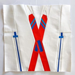 May include: A white fabric square with red and blue fabric strips sewn on top. The red strips are crossed over each other and the blue strips are sewn on the sides of the square.