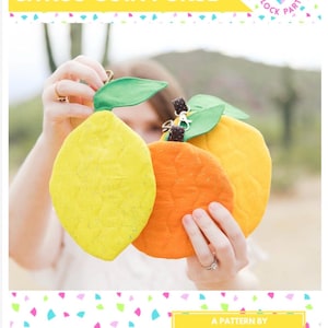 Pode incluir: Uma carteira de moedas de citrinos feita à mão em forma de limão, laranja e toranja. As carteiras de limão amarelo, laranja e toranja têm detalhes de folhas verdes e pequenos caules castanhos. O texto "CITRUS COIN PURSE" está na parte superior da imagem.