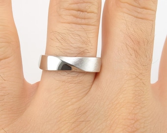 May include: A silver ring with a unique, twisted design. The ring is shown on a finger, highlighting its polished, metallic surface. The band has a flat profile with a subtle curve, creating a modern and elegant look. The ring is likely made of sterling silver.