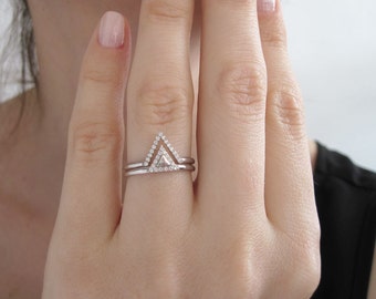 May include: A silver ring featuring a triangular design set with small diamonds. The ring is worn on the ring finger of a person's hand.