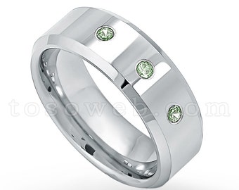 May include: A silver wedding band with three green gemstones set into the band.