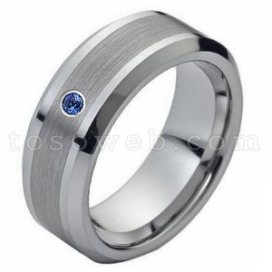 May include: A silver tungsten carbide ring with a brushed finish and a single blue sapphire gemstone.