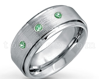 May include: A silver ring with a brushed finish and three green gemstones.