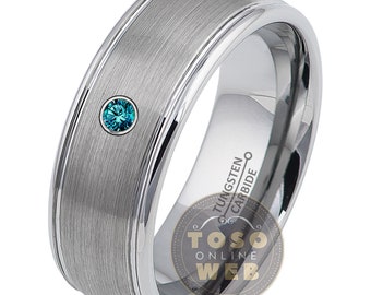 May include: A brushed silver tungsten carbide ring with a single blue gemstone set in the center. The ring has a beveled edge and is inscribed with "Tungsten Carbide".