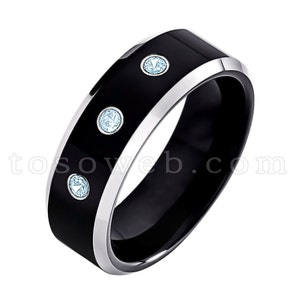 May include: A black tungsten carbide ring with a silver band and three blue gemstones.