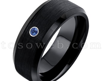 Pode incluir: Um anel de carboneto de tungstênio preto com acabamento escovado e uma única pedra de safira azul.
