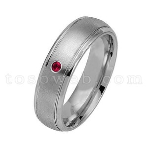 May include: A silver wedding band with a brushed finish and a single red gemstone.