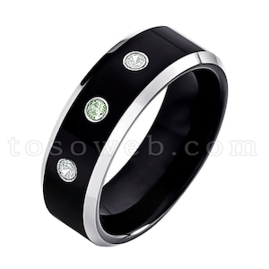 May include: A black tungsten carbide ring with a silver band and three gemstones. The ring has two green gemstones and one white gemstone.