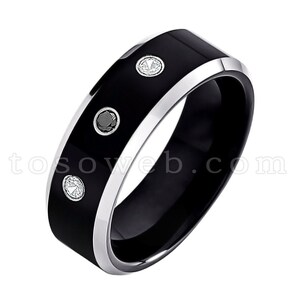 May include: A black tungsten carbide ring with a beveled edge and three small gemstones set into the band. The ring has a silver-colored band.