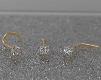 May include: Three gold nose rings with a clear gemstone in the center of each ring.