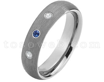 Pode incluir: Uma aliança de prata escovada com três pedras preciosas. A aliança tem dois pequenos diamantes brancos e um safira azul.