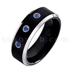 May include: A black tungsten carbide ring with a silver band and three blue sapphires.