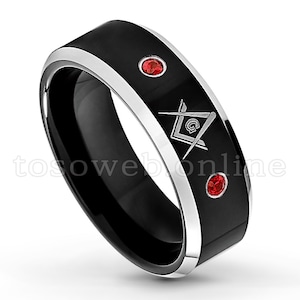 May include: A black and silver tungsten carbide ring with a silver Masonic symbol and two red gemstones.