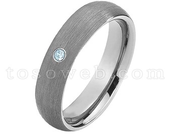 Pode incluir: Um anel prateado com acabamento escovado e uma pequena gema redonda azul clara. O anel tem uma banda interior polida e um design simples. O texto "tosoweb.com" é visível.