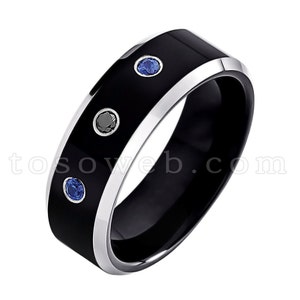 May include: A black tungsten carbide ring with a silver band and three gemstones. Two of the gemstones are blue and one is black.