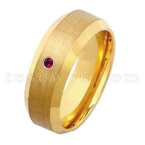 May include: A gold tungsten carbide ring with a brushed finish and a single red gemstone.