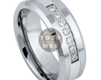 May include: A silver-colored ring with a row of clear, round gemstones set in a channel. The ring has a polished finish and a beveled edge design. The ring is a jewelry item.