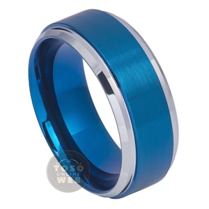 Pode incluir: Um anel de carboneto de tungsténio azul e prateado com uma borda chanfrada e um acabamento escovado.