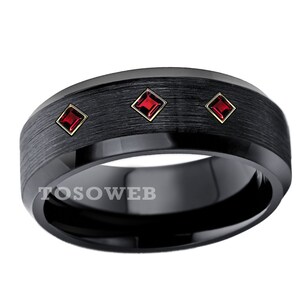 May include: A black tungsten carbide ring with three red square-shaped gemstones. The ring has a brushed finish.