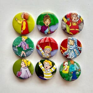 Puede incluir: Nueve botones redondos con ilustraciones coloridas de personajes de dibujos animados. Los botones muestran varias escenas y figuras, incluyendo una niña con un vestido rojo y un niño con gafas. Acabado brillante.