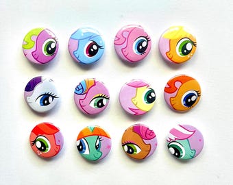 Può includere: Dodici spille rotonde disposte in tre file da quattro. Ogni spilla presenta il volto stilizzato e colorato di un pony dei cartoni animati con grandi occhi, in varie tonalità di rosa, blu, arancione, giallo, viola, rosso e verde.