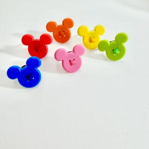 May include: Six colourful buttons in the shape of a mouse's head. The buttons are in red, orange, yellow, green, pink, and blue. Each button has a contrasting thread sewn through the centre.
