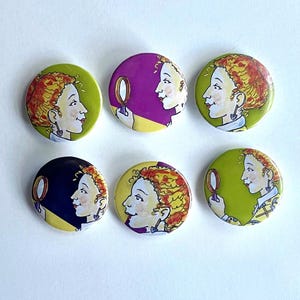 Puede incluir: Seis botones redondos con ilustraciones de una persona con cabello rizado rojo mirándose en un espejo de mano. Los botones tienen un fondo verde lima, morado, amarillo y azul marino. La persona lleva una camisa blanca y un pendiente en forma de corazón.