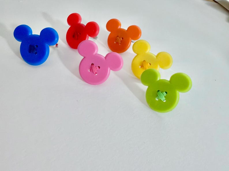 May include: Six colourful buttons in the shape of a mouse's head. The buttons are blue, red, orange, pink, yellow, and green, each with a contrasting thread detail. Suitable for sewing and craft projects.